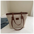 Detail of a large straw tote bag with brown faux leather trim on a white bed - Brown