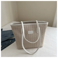 Detailed texture of beige woven straw tote bag with white leather straps on white bedding - White