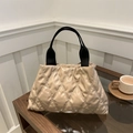 Borsa tote trapuntata beige con manici neri intrecciati su un tavolo di legno - Cachi