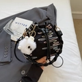 Black drawstring bucket bag with colorful zigzag embroidery and plush ball charm on a bed - Black With Rabbit Pendant