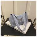 Detail of light blue pleated underarm bag with silver butterfly ornament on a book - Blue