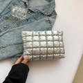 Dettaglio della borsa clutch argento trapuntata tenuta su sfondo denim azzurro - Argento