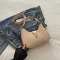 Bolso de hombro tipo montura beige con hebilla metálica dorada sobre fondo denim - Caqui