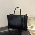 Borsa tote minimalista in pelle nera con scritte a rilievo e doppi manici sul divano - Nero