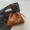 Brown quilted bucket bag with silver bow detail and drawstring closure on a grey suit - Brown