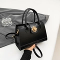 Elegant black crocodile-patterned tote bag with a golden floral lock on a gray suit background - Black