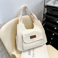 Minimalist beige canvas tote bag with outer pocket and brown leather patch on a chair - White