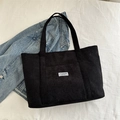 Bolso tote negro de pana con bolsillo frontal y etiqueta blanca de diseño moderno - Negro
