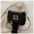 Detail of black quilted shoulder bag with gold clasp on beige blazer background - Black