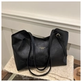 Detalle de bolso tote de cuero negro con letras doradas sobre fondo de punto beige - Negro