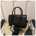 Dettaglio di una borsa nera in pelle con patta geometrica appoggiata su un maglione - Nero