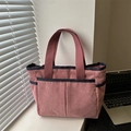 Pink corduroy tote bag with blue trim and front pockets shown in a cozy window setting - Pink