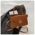 Dettaglio borsa in pelle caramello con chiusura floreale dorata su un blazer grigio - Marrone