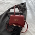 Burgundy PU leather crossbody bag with a gold bow buckle and unique curved base - Red