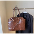 Dettaglio di una borsa tote marrone lucida con trama cerata e cinturini con fibbia su blazer - caffè