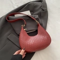 Bolso hobo de media luna roja trenzada con herrajes dorados sobre chaqueta gris - Rojo