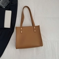 Brown faux leather tote bag with gold studs and shoulder straps on a textured surface - Brown