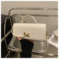 Detail of white woven texture crossbody bag with a golden bird clasp on a metal shelf - White