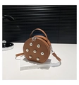 Close-up of brown round crossbody bag with silver studs on a white book prop - Brown
