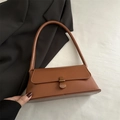Bolso baguette de cuero marrón con hebilla de metal vintage sobre fondo de tela blanca - Marrón Claro