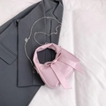 Bolso tipo cubo rosa con lazo y cadena plateada sobre fondo de chaqueta gris - Rosa
