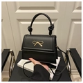 Close-up of black matte leather handbag featuring a gold bow clasp and knotted handle - Black