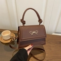 Dunkelbraune Handtasche mit goldener Schleife und Knotengriff auf dem Tisch platziert - Braun