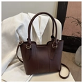 Detail of a dark brown leather bucket bag with gold hardware on a white chair - Brown