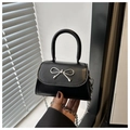 Close-up of black mini crossbody bag with silver bow accent and metal chain strap - Black