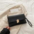 Piccola borsa nera con strisce orizzontali e fibbia dorata su un blazer beige - Nero