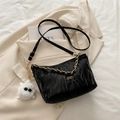 Black pleated crossbody bag with gold chain and plush charm on a beige blazer - With Pendant / Black