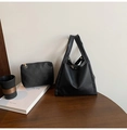 Detail of black pebbled leather bucket bag set with gold hardware on wooden desk - Black