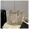 Detalle de bolso tote beige trenzado con cadenas plateadas y textura de espiga elegante - Blanco Roto