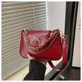Detail of wine red leather underarm bag featuring a golden bow buckle and chain tassels - Red