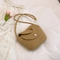 Bolso bandolera de paja tejida beige con botón de perla sobre fondo de tela blanca - Caqui