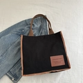Sac cabas en velours côtelé noir avec sangles brunes et écusson sur fond texturé blanc - Noir