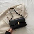 Classic black leather underarm bag with gold lock closure on a cream blazer - Black