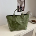 Bolso tote grande verde oliva brillante con texto blanco sobre mesa minimalista - Verde