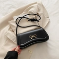 Elegante bolso baguette de cuero negro con hebilla de lazo dorado sobre blazer beige - Negro