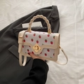 White textured crossbody bag with red strawberry print and golden flower twist lock - White