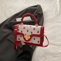 Elegant white crossbody bag with red strawberry print and golden floral clasp detail - Red