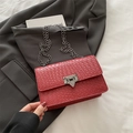 Red woven crossbody bag with silver chain strap and metal buckle on grey blazer - Red
