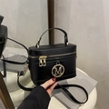 Sac à main boîte noir minimaliste avec logo M doré et bandoulière réglable sur fond studio - Noir