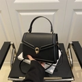Minimalist black matte leather handbag with gold hardware and shoulder strap on a chair - Black