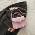 Elegant pink leather crossbody bag with gold buckle displayed on a grey blazer suit - Pink