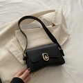 Elegante borsa a tracolla nera opaca con chiusura a rotazione dorata su un blazer - Nero