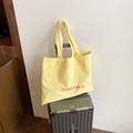 Bright yellow canvas tote bag with red letter print hanging on a suitcase handle - Yellow