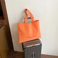 Orange nylon tote bag with red lettering on a silver suitcase handle for travel - Orange