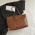 Caramel quilted tote bag with metal bow buckle and chain strap on a white texture background - Brown