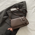 Dunkelbraune Baguette-Tasche mit Silberschnallen und Kette vor grauem Blazer-Hintergrund - Braun